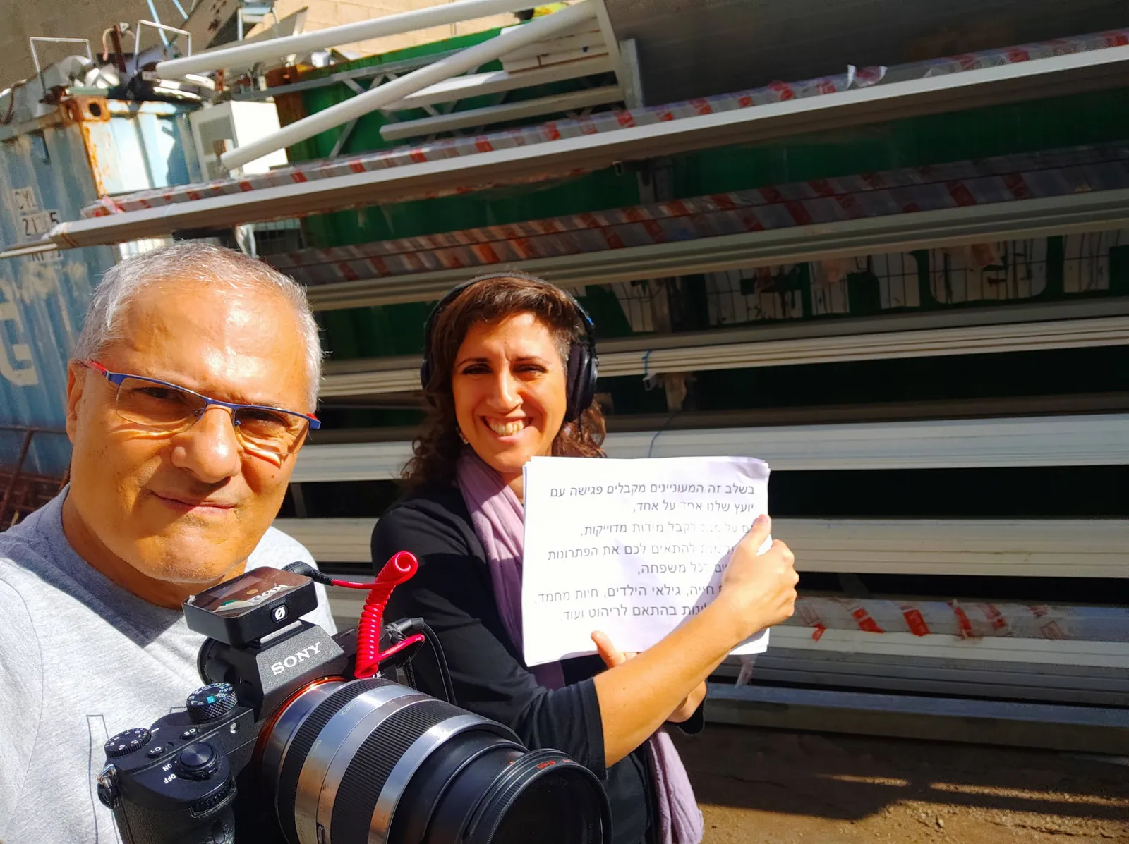 מיי מיי עם אוזניות ודף תסריט לצד צלם ומצלמת וידאו בלוקיישן תעשייתי